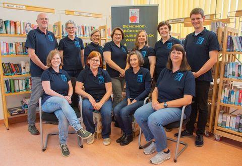 Büchereiteam - teils sitzend, teils stehend vor Regalen