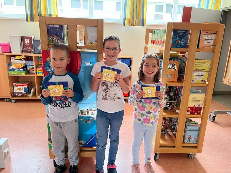 3 Kinder mit Gewinn vor Bücherregalen